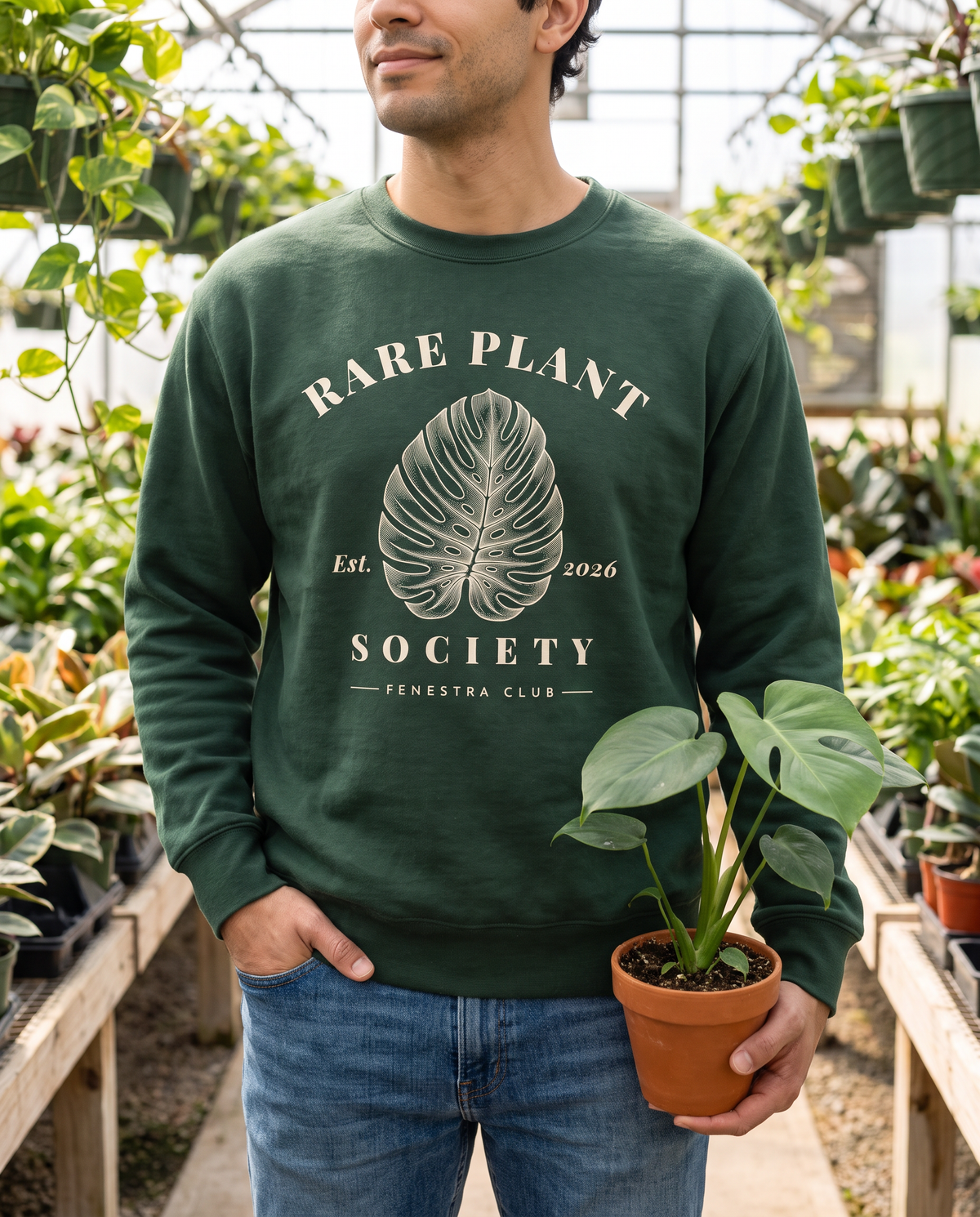 Man in a greenhouse wearing the Rare Plant Society crewneck sweatshirt in Forest Green
