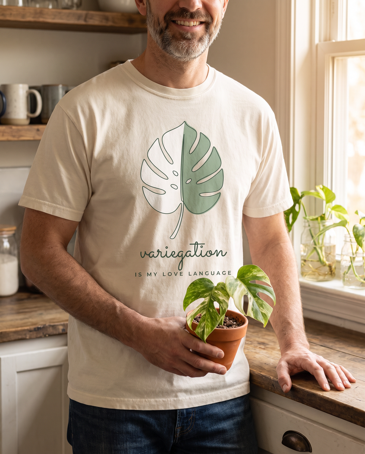 Man holding a variegated monstera, wearing the Variegation Is My Love Language tee in Ivory