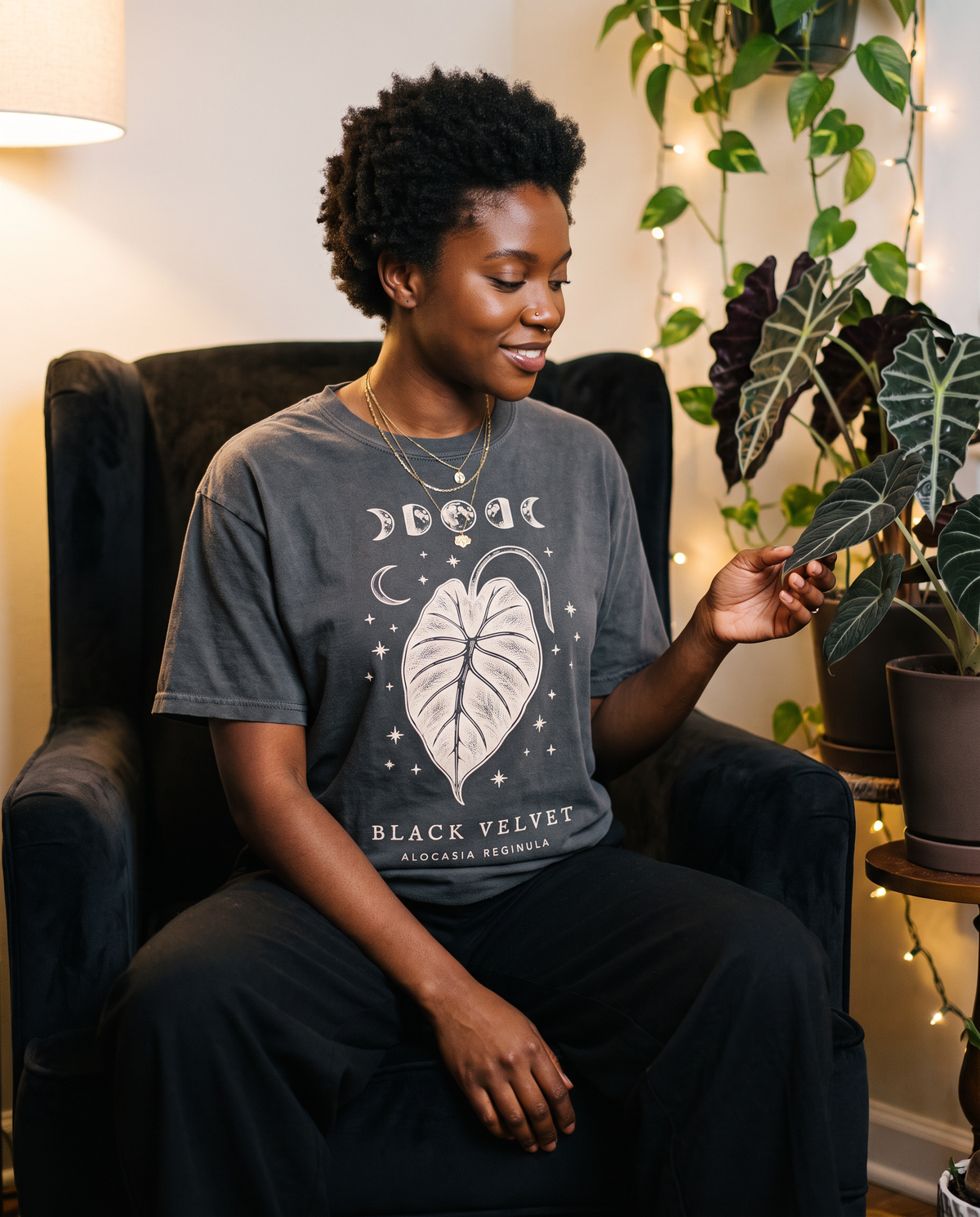 Woman touching a dark alocasia leaf, wearing the Black Velvet tee in Pepper